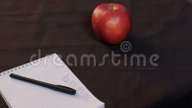 一个红<strong>苹果</strong>躺在黑色桌布上。 少年特写的手在桌上放下<strong>笔记本</strong>和笔..